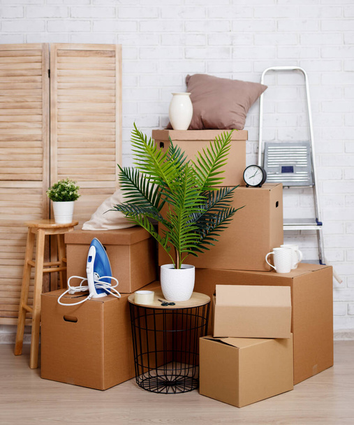 moving day concept - stacked cardboard boxes, houseplant and other domestic things over white brick wall background - Photo, Image