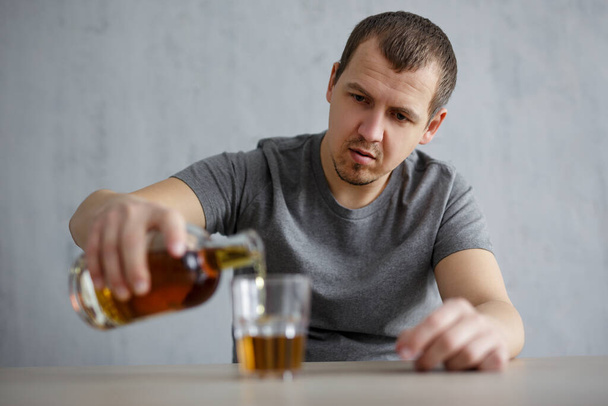 retrato del hombre vertiendo alcohol en vidrio sobre fondo gris - Foto, Imagen