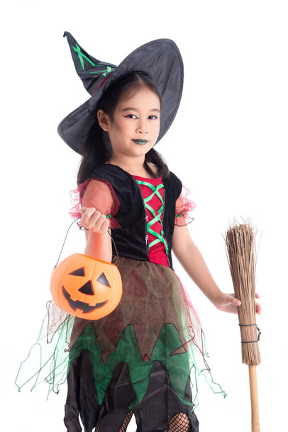 Egy kis ázsiai lány boszorkányjelmezben, aki tökvödröt és seprűt tart fehér háttér felett. Gyermek Halloween jelmez koncepció. - Fotó, kép