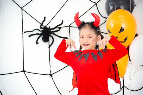 Pouco asiático menina no vermelho diabo vestido sorrindo no halloween decorado quarto. - Foto, Imagem
