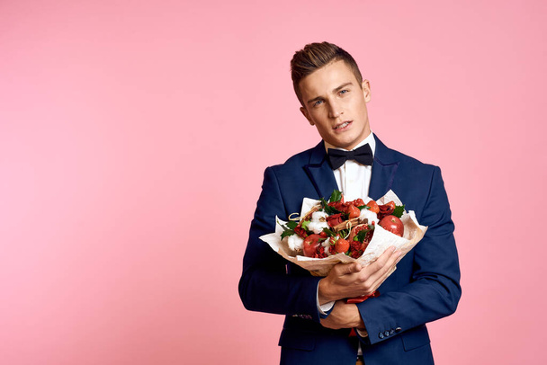 Handsome man in a classic suit with a bouquet of flowers on a pink background holidays bow tie model - Photo, Image