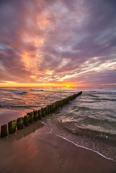 Γραφικό ηλιοβασίλεμα πάνω από τη Βαλτική Θάλασσα με ένα παλιό ξύλινο κυματοθραύστη στην παραλία. - Φωτογραφία, εικόνα