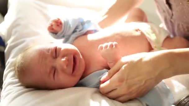 Liebevolle Mutter zieht Kleidung für ihr kleines Baby an - er beginnt zu weinen und die Frau umarmt ihn - Filmmaterial, Video