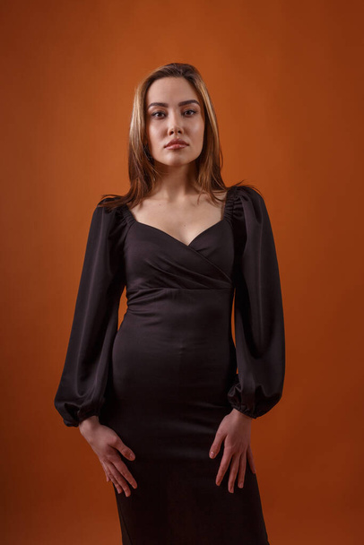 elegante modelo con vestido negro con escote profundo posando sobre fondo naranja - Foto, Imagen