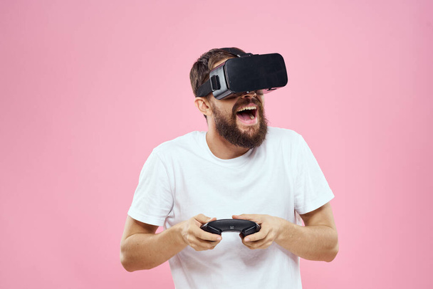 Man in virtual reality glasses joystick playing video lifestyle white t-shirt pink background - 写真・画像