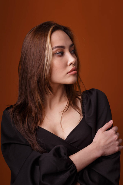 elegant model wearing black dress with deep neckline posing on orange background - Photo, Image