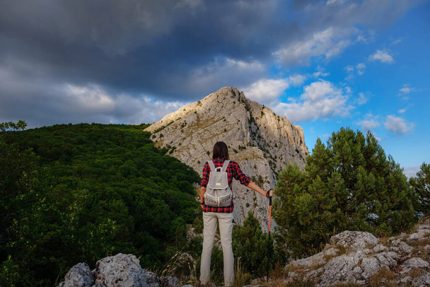 Adatta escursionista femminile con zaino e bastoni in piedi su una cresta rocciosa di montagna e cime in un concetto di stile di vita sano all'aperto - Foto, immagini