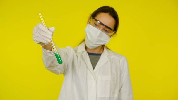 Врач в медицинской маске, очках и латексных перчатках смотрит на тесты в трубке - Фото, изображение