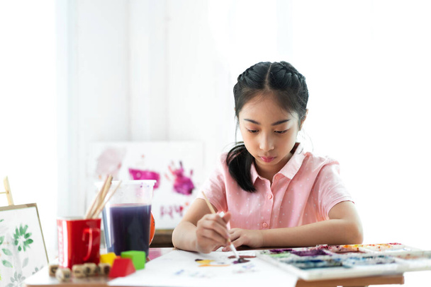 Küçük kız ressam evde renk paleti ve suluboya resimlerle tuvale resim çiziyor. - Fotoğraf, Görsel