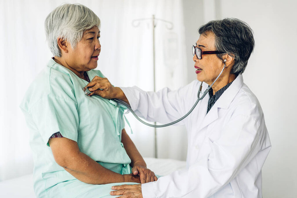 Medico senior femminile che consulta ed esamina una paziente anziana con stetoscopio in ospedale. assistenza sanitaria e medicina - Foto, immagini