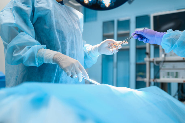 Женщина-хирург и ассистент выполняет хирургическую операцию в операционной. Врач в форме, медицинский работник клиники, медицина и здоровье, здравоохранение в больнице - Фото, изображение