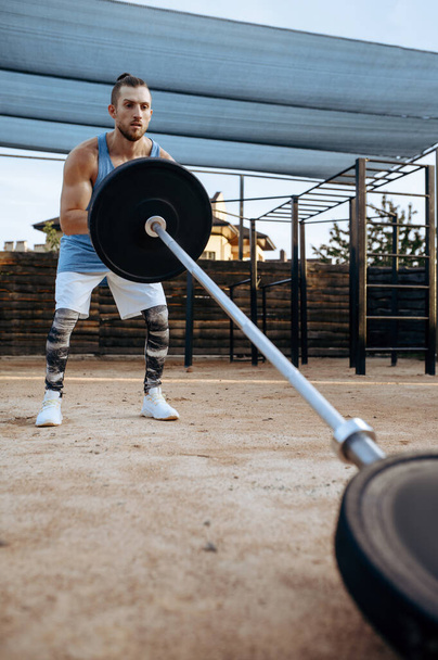 М'язистий чоловік готує ваги для вправ, тренування вулиць. Фітнес-тренування на спортивному майданчику на відкритому повітрі, чоловік накачує м'язи, активний міський спосіб життя
 - Фото, зображення