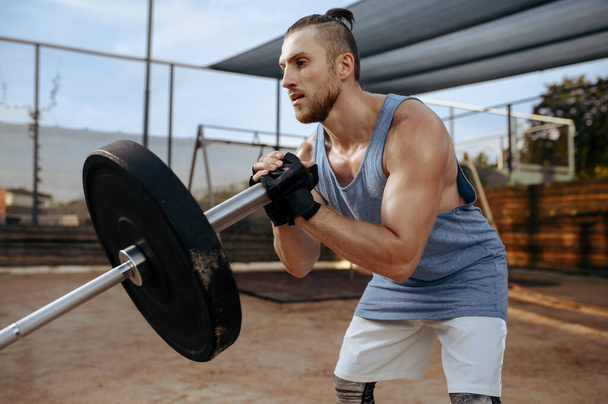 Muscular man prepares barbell weights for exercise, street workout. Fitness training on sports ground outdoor, male person pumps muscles - Photo, Image