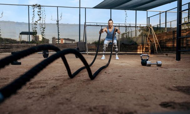 Strong man doing exercise with ropes, street workout, crossfit. Fitness training on sports ground outdoor, male person pumps muscles - Fotografie, Obrázek