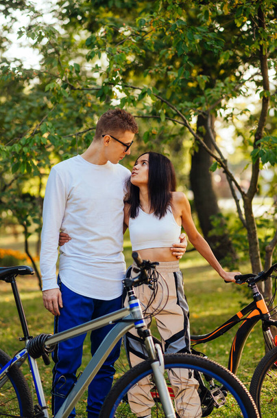 Portrait of stylish loving couple standing with bicycles in autumn park and hugging. Beautiful man and woman spend time in the park on a bike ride. Vertical. - Photo, Image