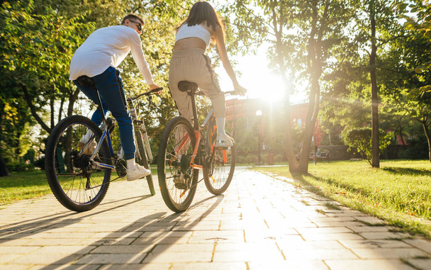 Стильная пара на велосипедах в осеннем парке на закате. Мужчина и женщина едут на велосипеде по аллее в парке. Вид сзади. - Фото, изображение