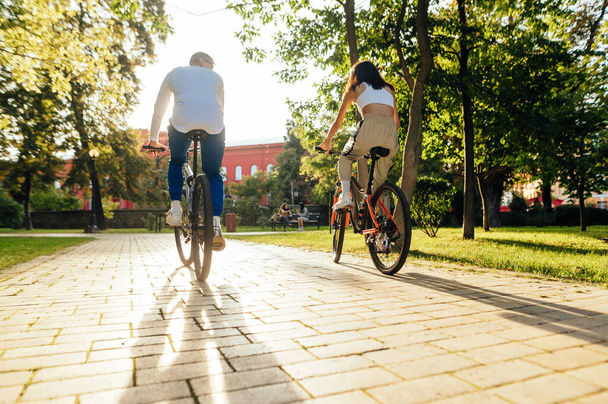 Стильная пара молодых людей катается в парке в осенний сезон на закате. Активный велоспорт в городе по выходным. Вид сзади. - Фото, изображение