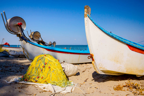 Куча коммерческих рыболовных сетей и катеров с механизмом спуска размещены на песчаном пляже. - Фото, изображение