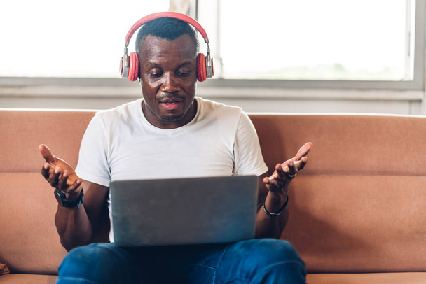 Nuori musta afrikkalainen mies rentouttava kannettavan tietokoneen työ- ja videoneuvottelussa kotona. Nuori luova afrikkalainen mies puhuu headset.work kotoa käsite - Valokuva, kuva