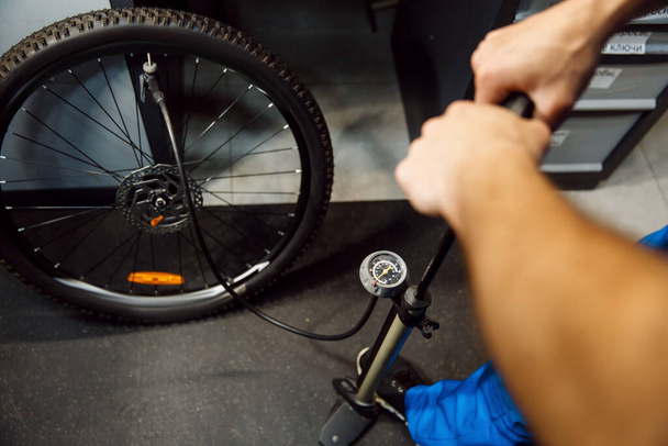 Bicycle assembly in workshop, man inflates the wheel. Mechanic in uniform fix problems with cycle, professional bike repairing service - Foto, afbeelding