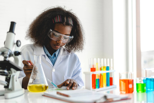 Studentessa afroamericana carina bambina che impara la ricerca e fa un esperimento chimico mentre fa analizzare e mescolare il liquido in vetro a lezione di scienza sul tavolo. - Foto, immagini