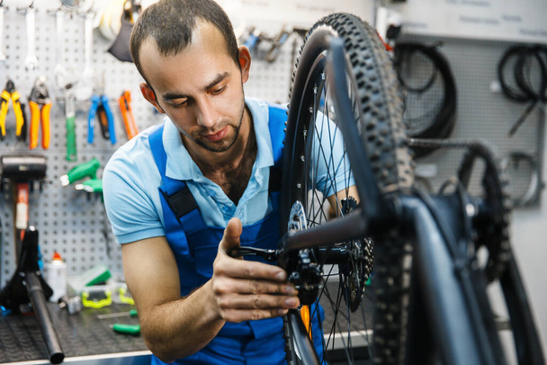 Montaż rowerowy w warsztacie, instalacja łańcuchowa. Mechanik w mundurze naprawić problemy z rowerem, profesjonalny serwis naprawy rowerów - Zdjęcie, obraz