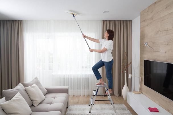 Frau putzt Decke mit Wischmopp. Hausfrau putzt Wohnzimmer - Foto, Bild