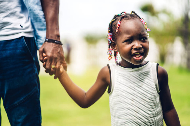 Портрет счастливой семьи чернокожих африканцев, отец которых держит маленькую африканскую девочку за руку в моменты хорошего времяпрепровождения в летнем парке дома - Фото, изображение