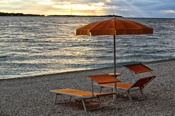 Pareja de tumbonas naranjas con sombrilla abierta en la playa vacía por la noche - Foto, Imagen
