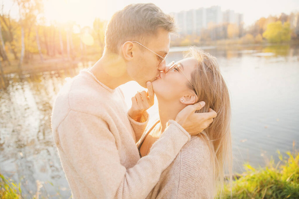 Loving couple in sunglasses round shape cuddle sweater and kiss against backdrop of autumn park - Photo, Image