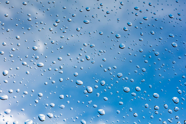 σταγόνες βροχής στο παράθυρο σε έναν γαλάζιο ουρανό με σύννεφα - Φωτογραφία, εικόνα