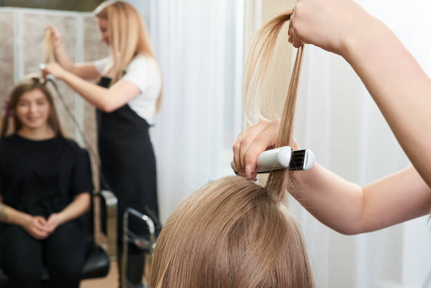 Hairstylist working on woman client with crimper - Photo, Image