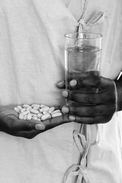 Studio schot van jonge Afrikaanse man als ziekenhuis patiënt geïsoleerd tegen witte achtergrond in zwart-wit - Foto, afbeelding