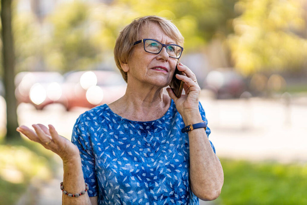 Stressed senior woman using mobile phone outdoors - Photo, Image