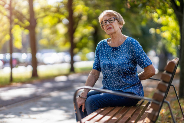 Senior woman with back pain having difficulty to get up from the bench - Photo, image