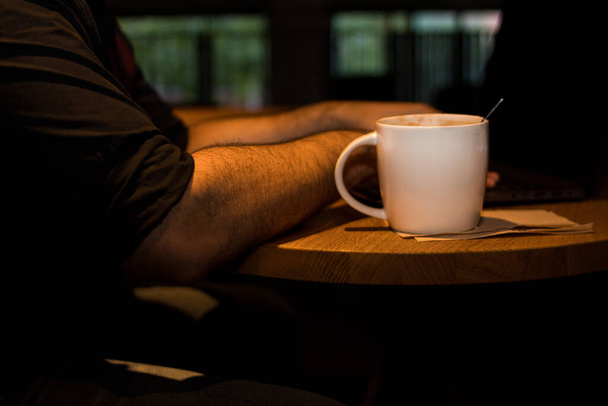 Ordinateur portable sur une table en bois dans un café avec une tasse de café et un téléphone à côté - Photo, image