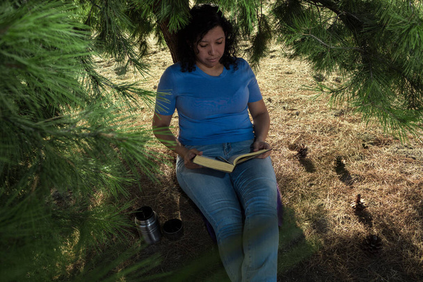 Běloška v džínách a modrém svetru, čte si na poli černou knihu s termoskou po boku - Fotografie, Obrázek