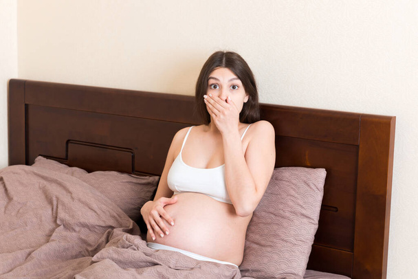 Вагітна страждає від нудоти. Симптоми вагітності, очікування токсикозу. Молода блювання жінка сидить у ліжку. концепція батьківства
. - Фото, зображення