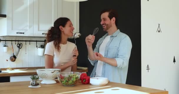 Couple holding ladle and beater like microphones singing in kitchen - Video