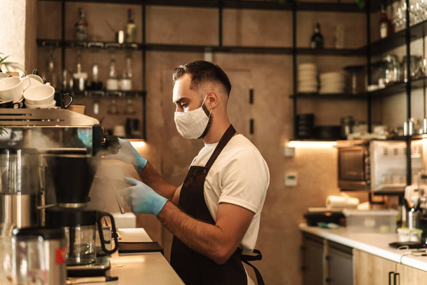 barista equipped with a protective mask for the virus, prepares and serves coffee in disposable cups - Фото, зображення
