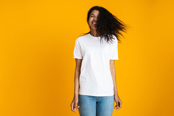 Portrait of an excited young african woman in casual wear standing isolated over yellow background, shaking her head - Foto, Imagen