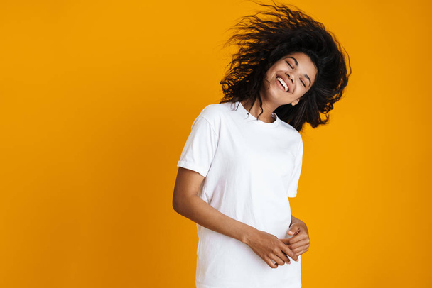 Portrait of an excited young african woman in casual wear standing isolated over yellow background, shaking her head - Foto, afbeelding