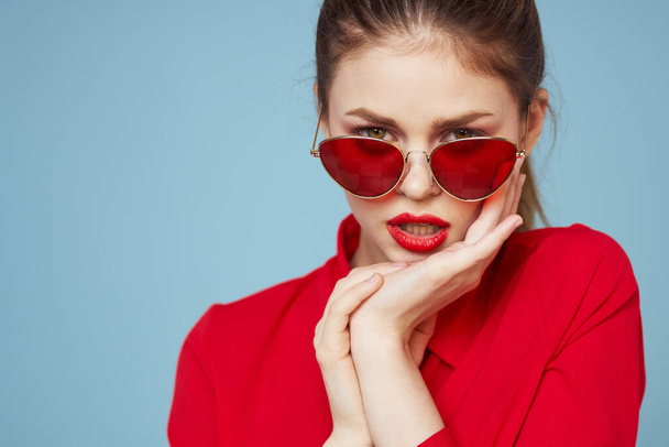 Beautiful woman in dark glasses red shirt bright makeup emotions attractive look blue background - Photo, Image