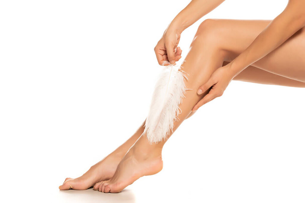 Frau berührt ihre Beine mit weißer Feder auf weißem Hintergrund - Foto, Bild