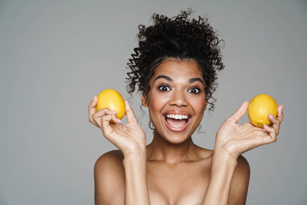 Image of excited shirtless african american woman posing with lemons isolated over grey wall - Foto, Imagen