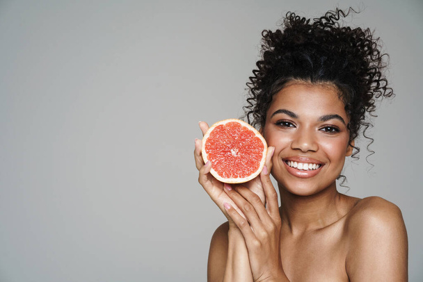 Image of shirtless african american woman smiling while posing with grapefruit isolated over grey wall - 写真・画像