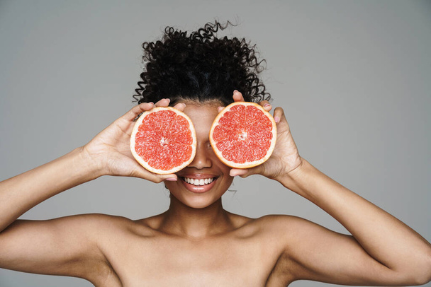 Image of shirtless african american woman smiling while posing with grapefruit isolated over grey wall - Foto, afbeelding