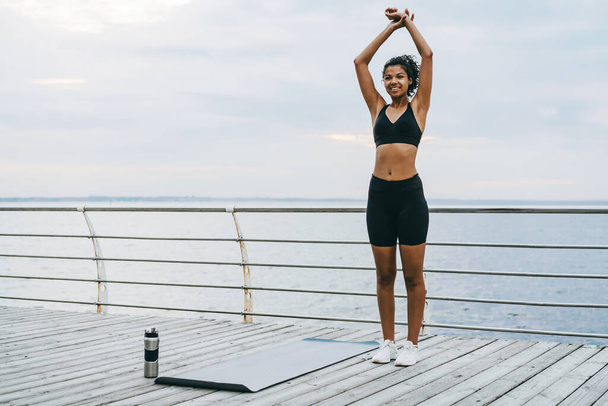 Image of smiling african american sportswoman doing exercise while working out on mat at promenade - Fotó, kép