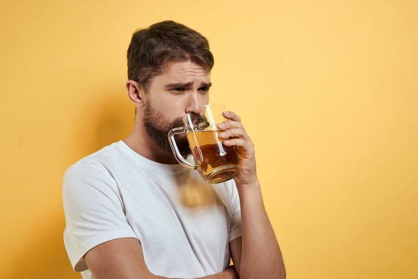 Hombre con una taza de cerveza diversión alcohol estilo de vida blanco camiseta amarillo aislado fondo - Foto, imagen