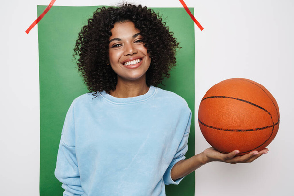 Image of pleased african american woman smiling while posing with basketball isolated over multicolored background - Valokuva, kuva